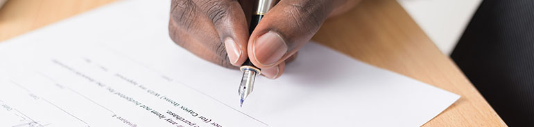 person holding pen to sign paper document