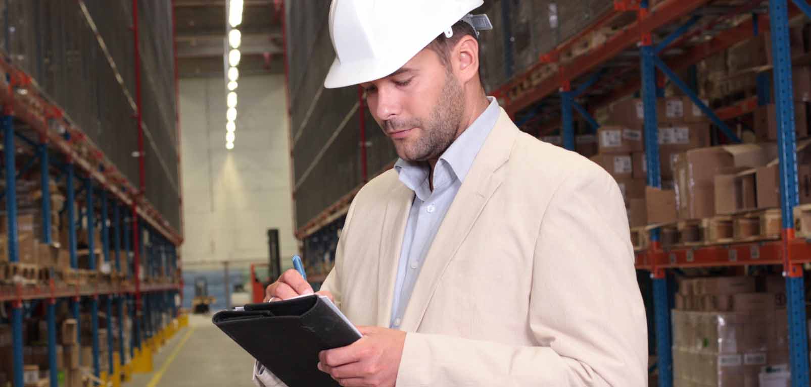 man wearing helmet and writing notes in a warehouse to illustrate new ppe regulations for 2022