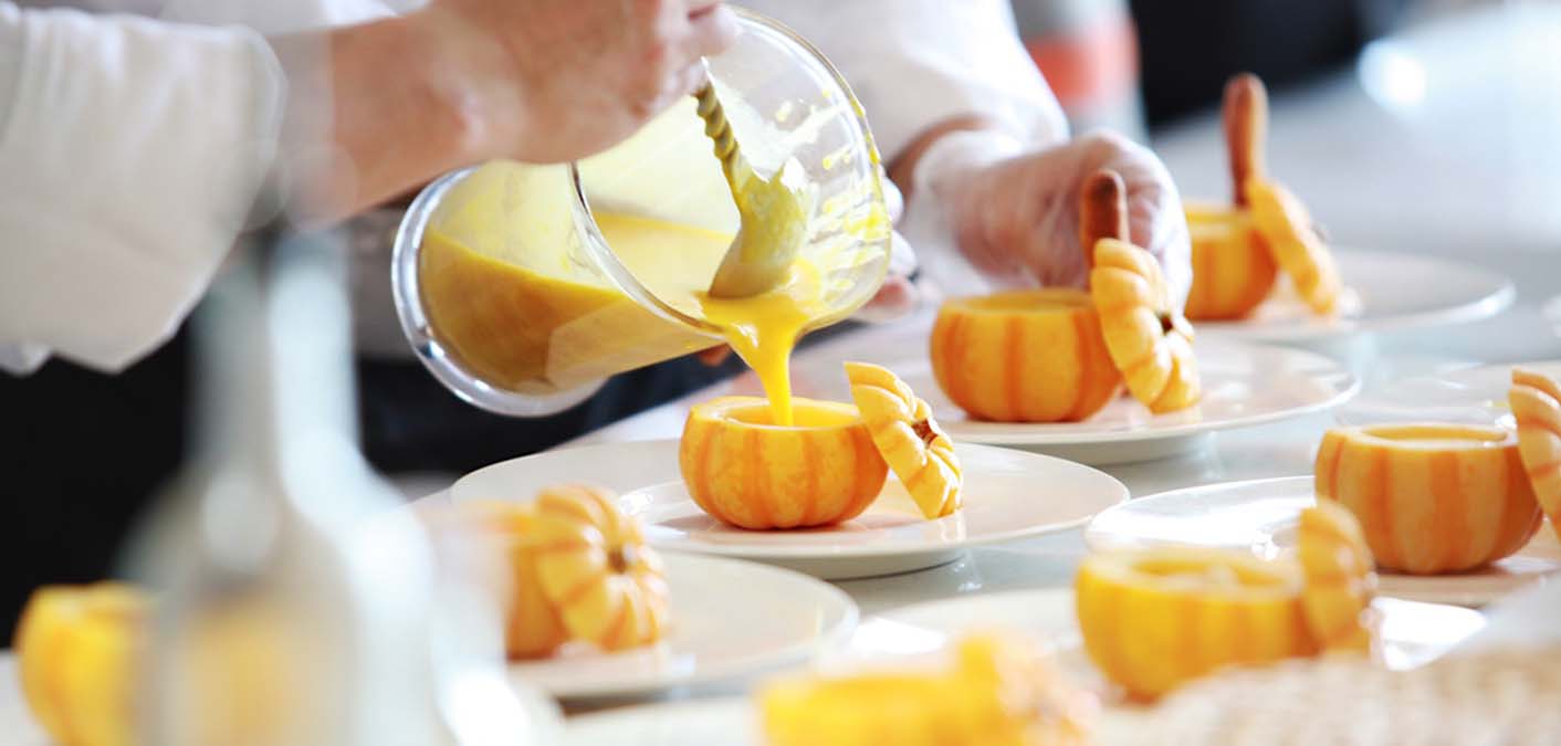 chef pouring pumpkin soup into small pumpkins on dishes to illustrate cooking
