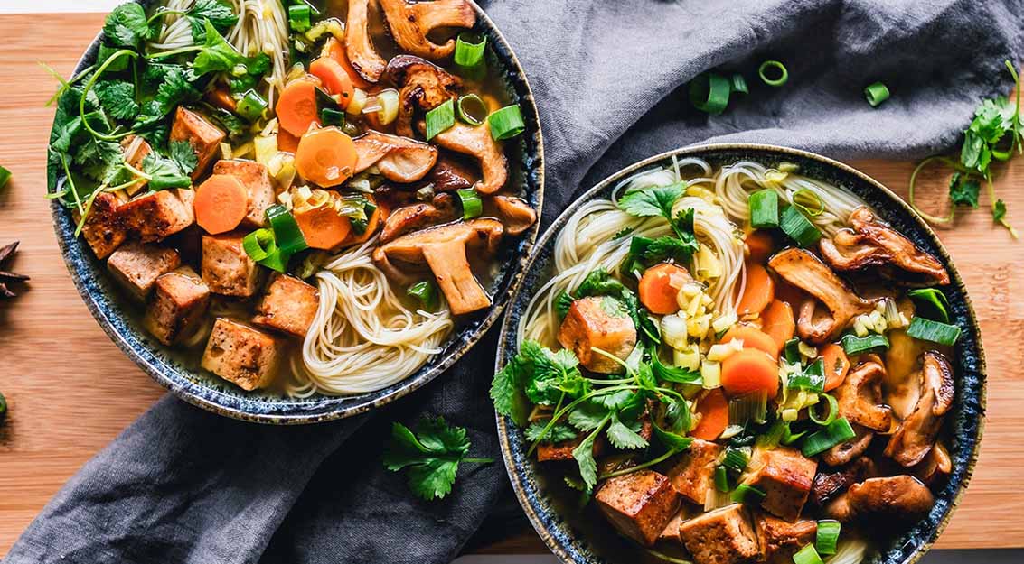 food bowls with noodles and vegetables on wooden table