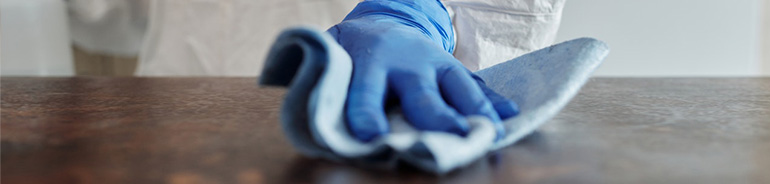 person wearing disposable gloves cleaning surface with a blue wipe