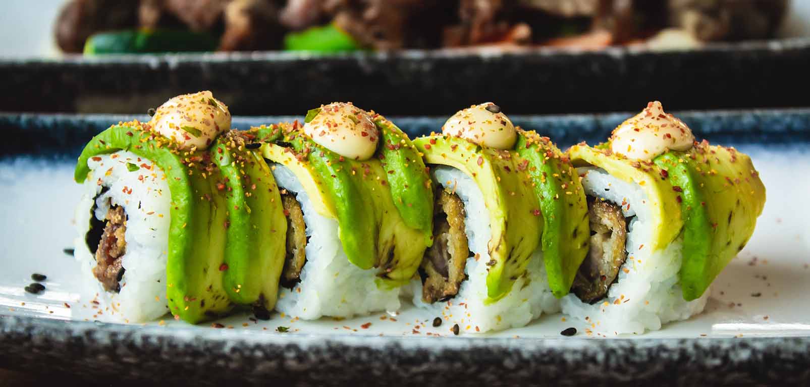 restaurant sushi with rice, avocado, seeds and sauces on a plate