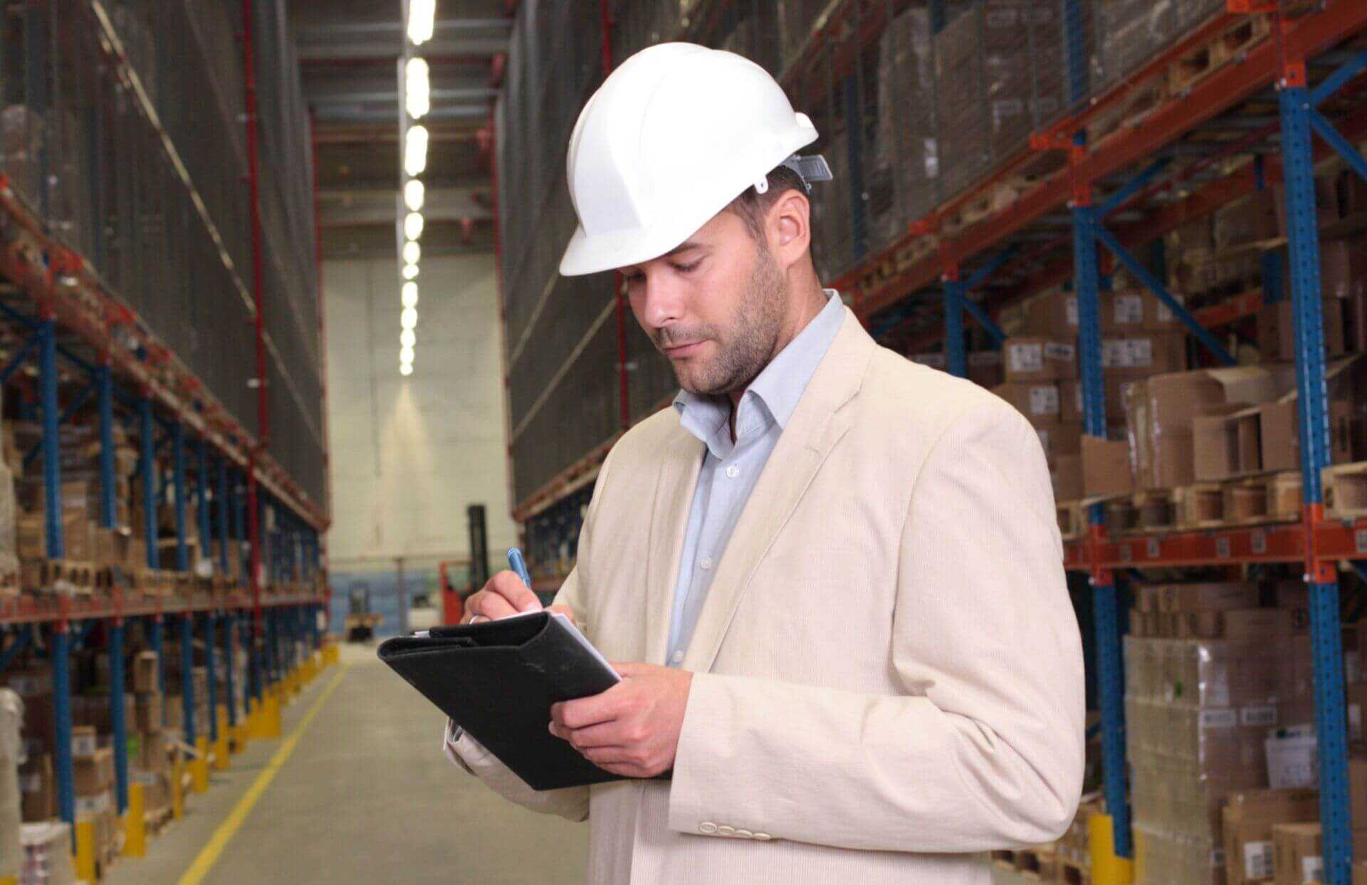person working and taking notes inside a warehouse to illustrate health & safety risk assessments
